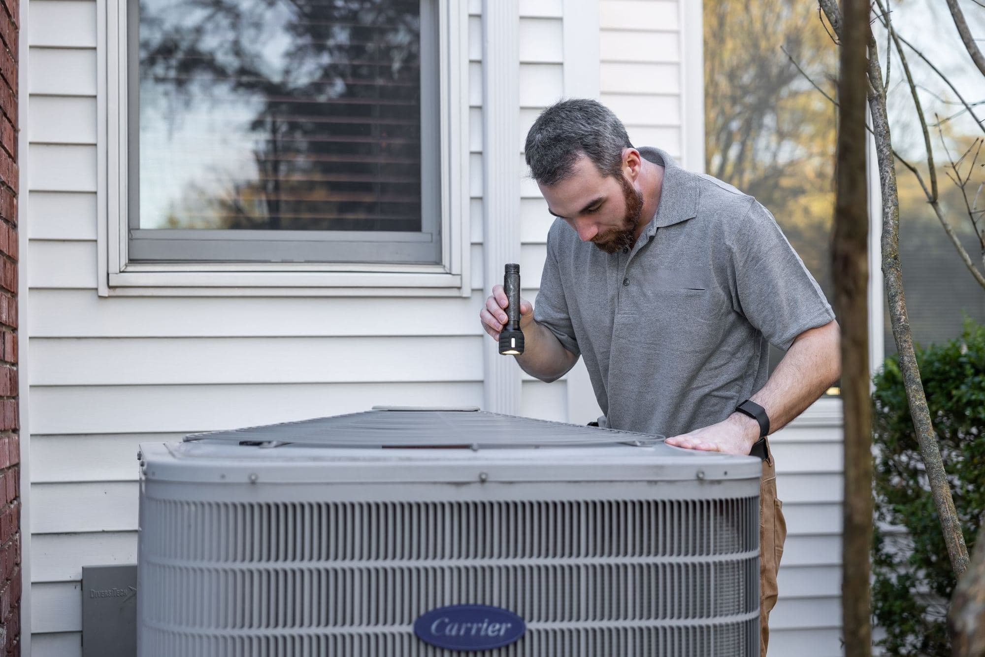 Technician inspecting a residential AC condenser beside a house